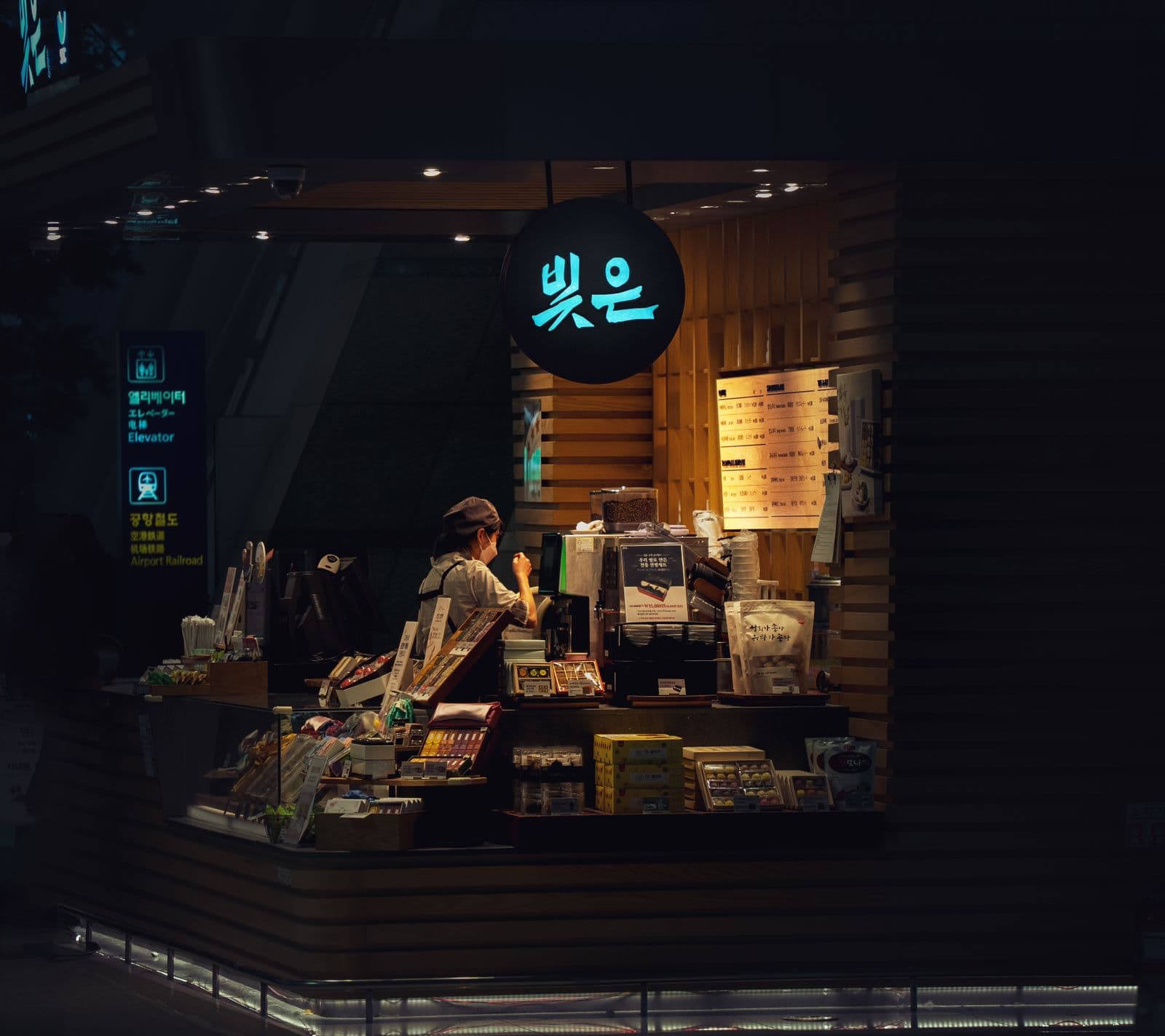 A small shop counter lit against the dark, one person working behind it at night